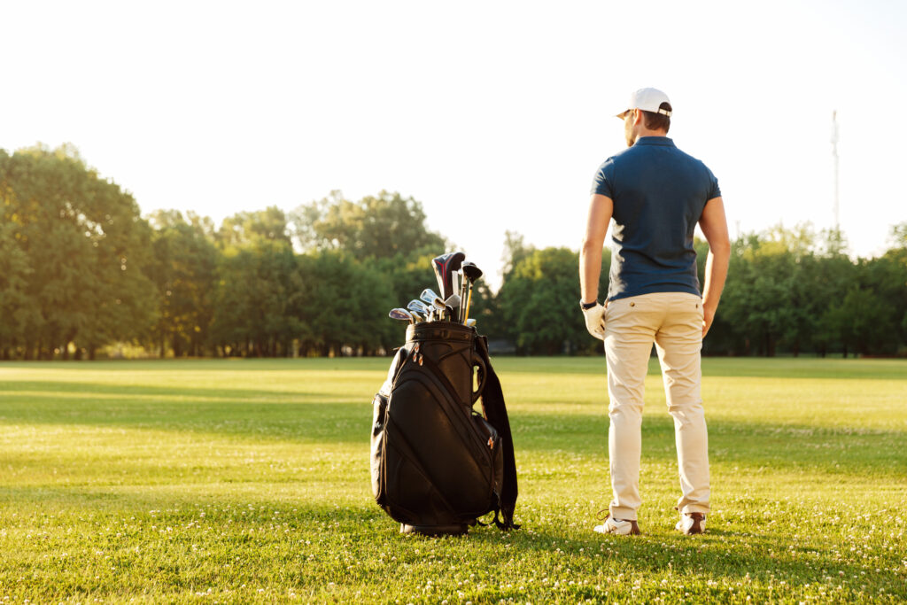 Golfer standing on a golf course, preparing for a round with clubs nearby.